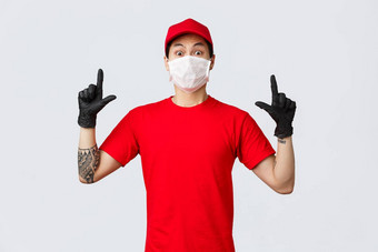 惊讶年轻的亚洲交付的家伙公司统一的红色的t恤帽盯着相机深刻的印象震惊了指出手指穿保护手套医疗面具工作