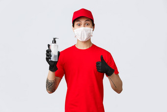 逗乐交付男人。红色的帽t恤使翘拇指标志穿保护手套医疗面具提供客户公司工人手消<strong>毒液</strong>概念非接触式安全交付