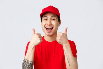交付非接触式订单购物概念支持快乐的年轻的亚洲快递红色的统一的帽t恤显示竖起大拇指批准推荐交付服务灰色背景