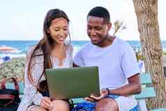 年轻的夫妇移动PC屏幕坐着板凳上海滩
