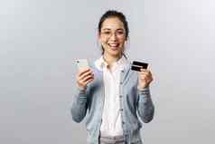 快乐的年轻的亚洲女人推荐银行订单在线使互联网购买交付应用程序持有信贷卡智能手机微笑满意灰色背景