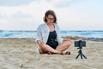 中间岁的女人坐着海滩智能手机<strong>视频</strong>调用