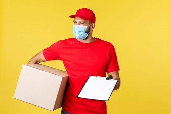 表达交付流感大流行科维德安全航运购物概念热情的英俊的快递红色的统一的医疗面具手套持有包盒子给剪贴板形式标志