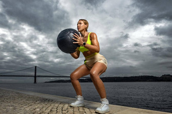 女人健<strong>身穿</strong>锻炼重医学球在户外运动女孩适合身体<strong>运动服</strong>装摆姿势天空背景