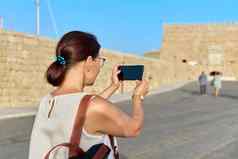 女人旅游采取照片智能手机古老的历史堡垒海滨