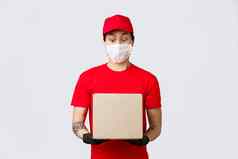 惊讶亚洲交付的家伙盯着包裹奇怪的噪音快递穿红色的帽t恤统一的保护手套医疗面具给客户端订单科维德self-quarantine