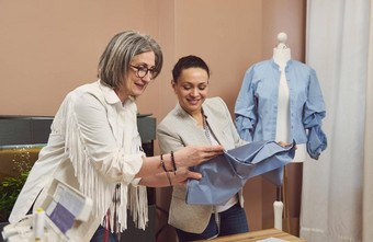 女裁缝工作熟练的裁缝织物讨论质量纺织的同事们现代缝纫讲习班改善生产过程