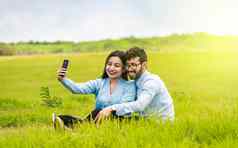 微笑夫妇爱坐着草采取自拍年轻的夫妇爱采取自拍场人爱采取自拍场智能手机