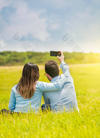 人爱采取自拍场智能手机微笑夫妇爱坐着草采取自拍年轻的夫妇爱采取自拍场