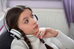 深思熟虑的年轻的女孩听音乐无线耳机