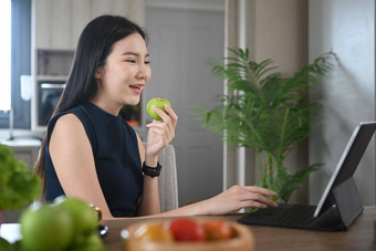 快乐的年轻的女人吃<strong>苹果电脑</strong>平板电脑厨房早餐