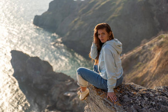 女人旅游享受日落海山景观坐在在户外岩石海穿牛仔裤蓝色的连帽衫<strong>健康</strong>的生活方式<strong>和谐</strong>冥想