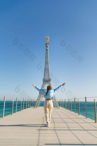 大模型埃菲尔铁塔塔海滩女人走码头塔穿蓝色的夹克白色牛仔裤