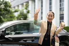 友好的亚洲高级夫人挥舞着手问候快乐微笑下车奢侈品车