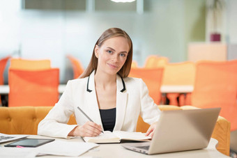 年轻的业务女人白色夹克西装桌子上移动PC相机使笔记金发女郎模型女蓝色的眼睛摆姿势业务西装办公室业务概念