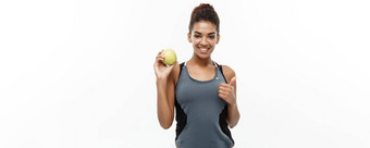 健康的健身概念美丽的美国非洲夫人灰色健身衣服持有绿色苹果孤立的白色背景