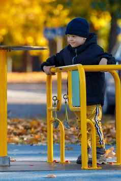 男孩玩操场上公园孩子旋转黄色的旋转木马秋天季节明亮的黄色的树背景垂直照片