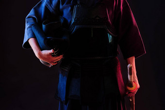 剑道战斗机穿护甲传统的和服持有头盔shinai竹子剑摆姿势黑色的背景关闭