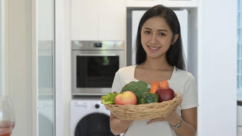 漂亮的年轻的女人持有柳条篮子新鲜的有机蔬菜水果站首页厨房