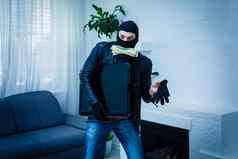 强盗男人。穿着黑色的连帽衫站伪装脸持有很多钱手偷了大量小偷男人。偷了