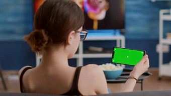 年轻的女人持有水平智能<strong>手机</strong>绿色屏幕流媒体应用程序看视频<strong>内容</strong>