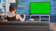 静态三脚架拍摄玩家女孩持有无线手柄玩行动控制台视频游戏绿色屏幕