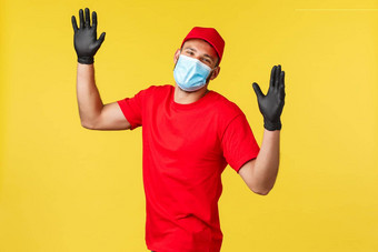 表达交付流感大流行科维德安全航运在线购物概念友好的快乐的快递红色的统一的帽t恤穿安全医疗面具手套挥舞着相机