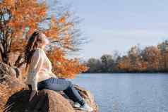 深思熟虑的浪漫的女人坐着岩石河银行日落秋天一天
