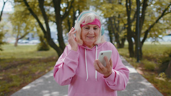 运动高级体育运动跑步者女人穿耳机听音乐智能手机早....公园