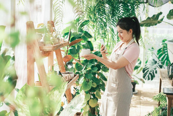 微笑年轻的女人采取智能<strong>手机图</strong>片植物小商店