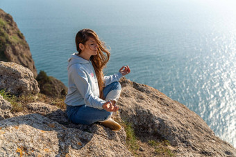 女人旅游享受日落海山景观坐在在户外岩石海穿牛仔裤蓝色的连帽衫<strong>健康</strong>的生活方式<strong>和谐</strong>冥想