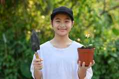 快乐的亚洲女孩持有花园铲盆栽植物站模糊绿色自然背景地球一天生态概念