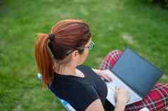 女人坐在公园类型电脑购物在线女孩维护社会距离作品在户外移动PC学生研究远程