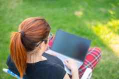女人坐在公园类型电脑购物在线女孩维护社会距离作品在户外移动PC学生研究远程