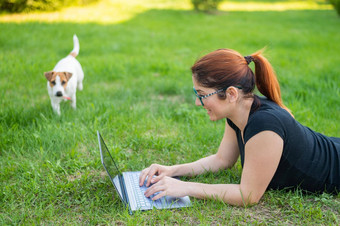 女人眼镜谎言绿色草公园狗女孩博主维护社会距离维护博客在户外学生研究远程移动PC