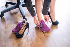 特写镜头腿办公室女员工脚疼痛女人高黑色的仿麂皮高跟鞋舒适的鞋子女孩需要鞋子把紫色的运行鞋子