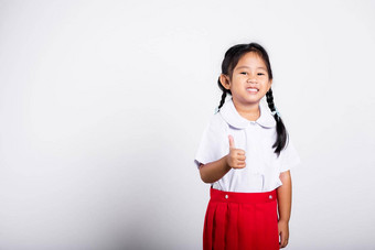 亚洲可爱的蹒跚学步的微笑快乐穿学生泰国统一的红色的裙子显示拇指手指
