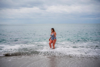 丰满女人洗澡西装进入水冲浪海滩灰色的天空云游泳冬天
