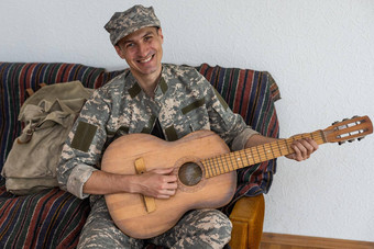 快乐的微笑年轻的军事男人。穿卡其色统一的持有吉他