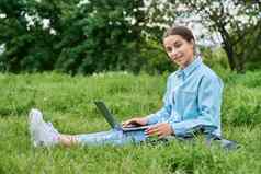 十几岁的女孩高学校学生移动PC坐着绿色草