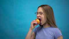 少年女孩牙套牙齿吃杏蓝色的背景女孩彩色的牙套咬杏