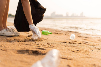 志愿者女人挑选塑料瓶垃圾塑料袋黑色的清洁海滩