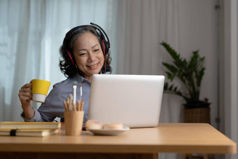 快乐高级亚洲女人穿耳机听歌曲移动PC生活房间舒适的首页