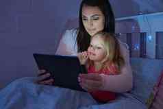 分钟妈妈拍摄妈妈。女儿坐着床上阅读睡觉前故事数字平板电脑