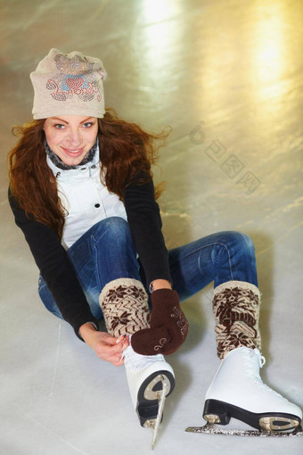 准备好了减少冰肖像有吸引力的年轻的女人坐着冰溜冰场系鞋带冰溜冰鞋