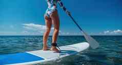 健康的快乐适合女人比基尼放松冲浪板浮动清晰的绿松石海水休闲体育站桨登机夏天有趣的假期旅行活跃的生活方式