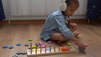 快乐学前教育没有牙齿的女孩玩彩色的木玩具孩子们学习数玩教数字首页孩子听音乐大白色耳机童年教育