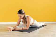年轻的女人坐着线瑜伽工作室照片运动型女人练习瑜伽坐着地板上拉伸分裂腿孤立的黄色的颜色背景