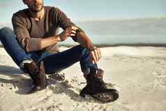 海边时刻男人。穿牛仔裤靴子坐着海滩