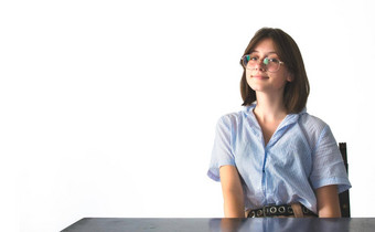 年轻的漂亮的女<strong>学生穿</strong>眼镜坐着桌子上纯白色背景